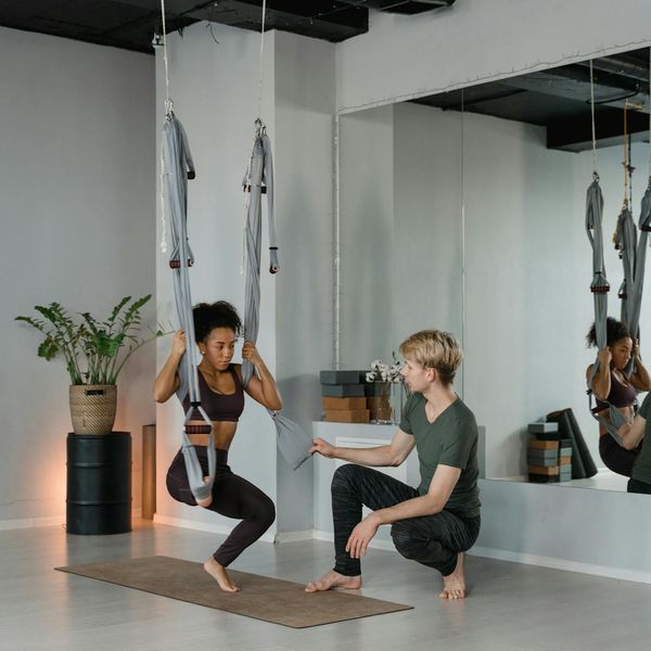 An instructor gently guiding a student in a correct yoga posture in a bright studio.